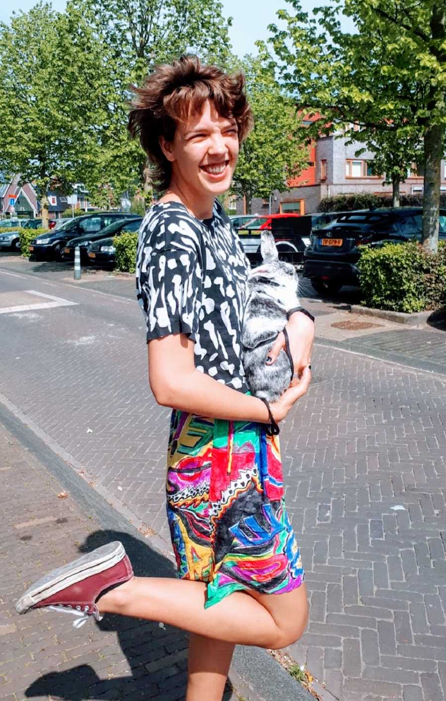 A person wearing a colorful skirt stands in the street holding a rabbit