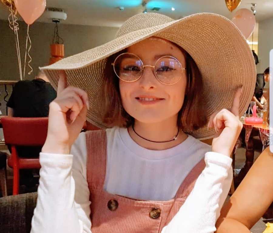 A woman wearing overalls and a large sunhat sits at a table