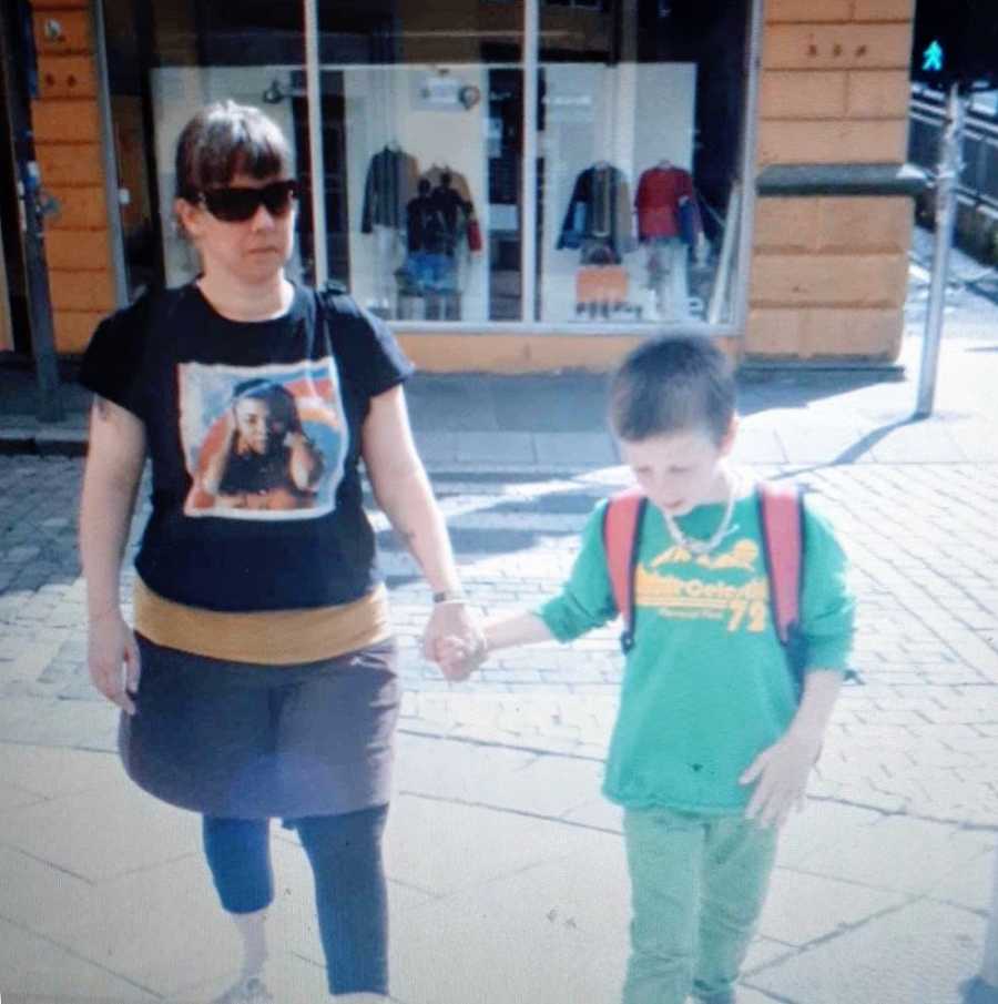 A nonbinary person and their son walking while holding hands