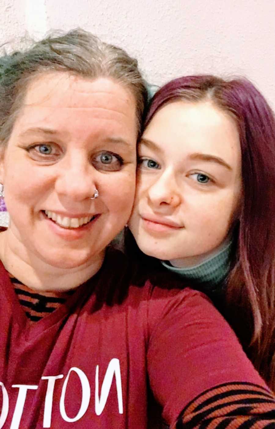 A nonbinary person and their daughter with faces pressed together for a photo