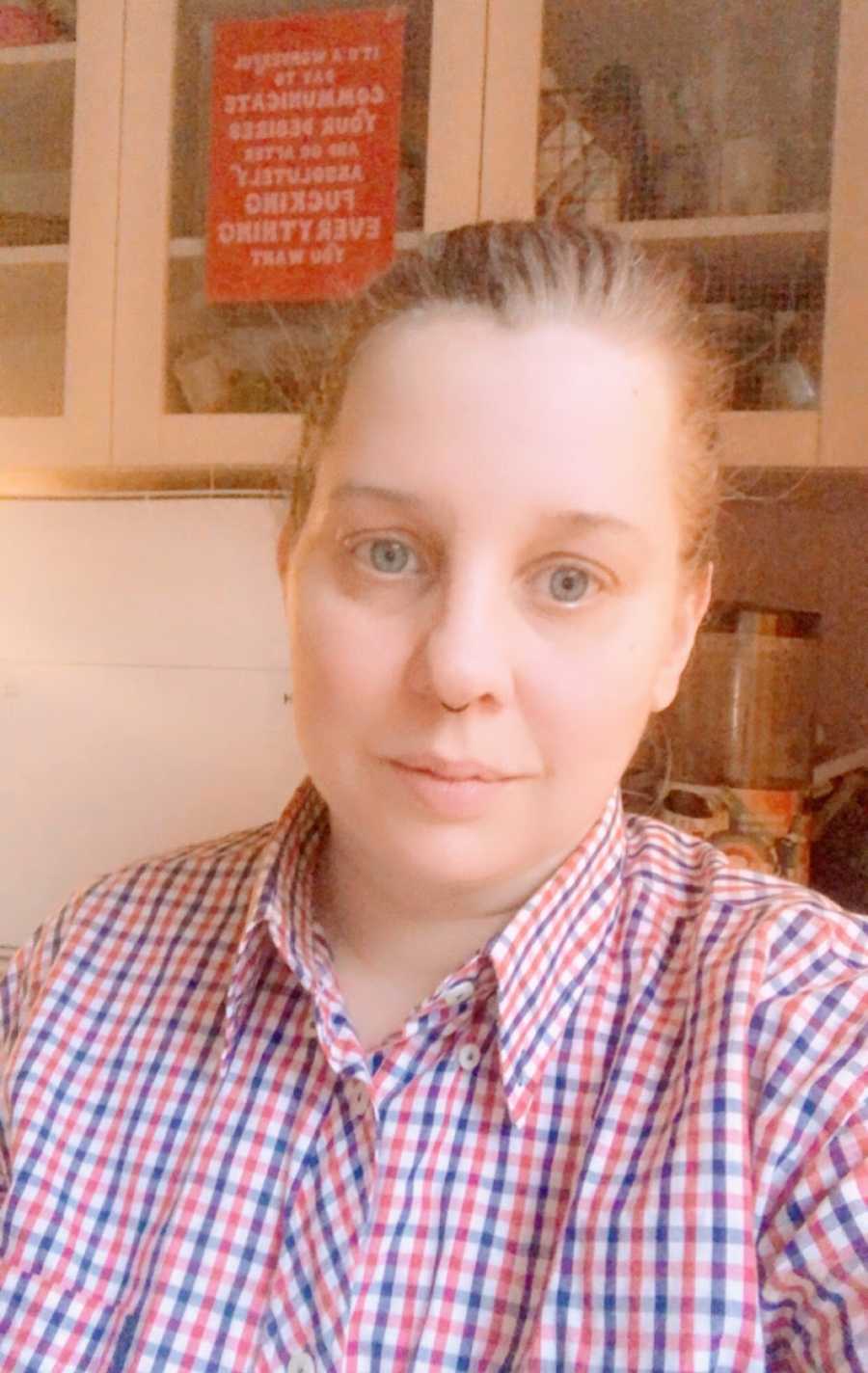 A nonbinary person wearing a red and blue checkered shirt