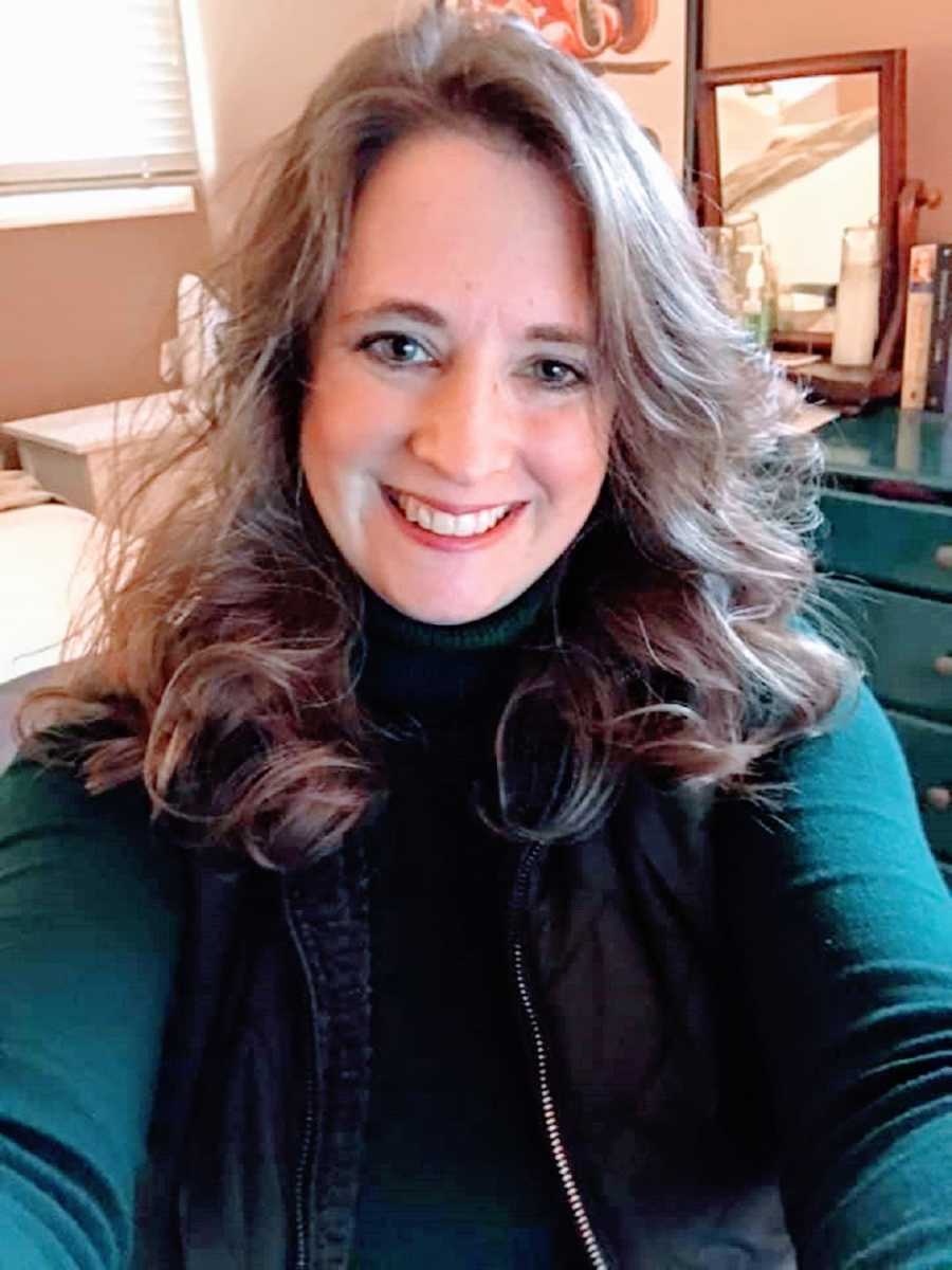 A woman with long wavy hair sits in a bedroom 