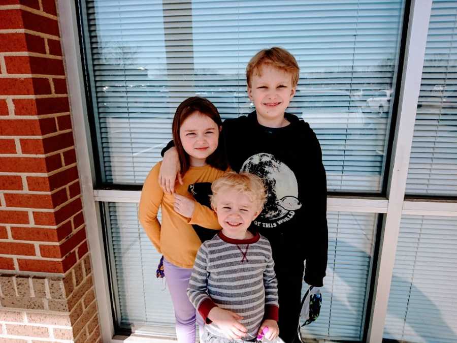 Three siblings stand together near a window