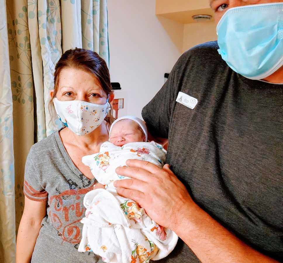 Parents hold their newborn baby while wearing masks