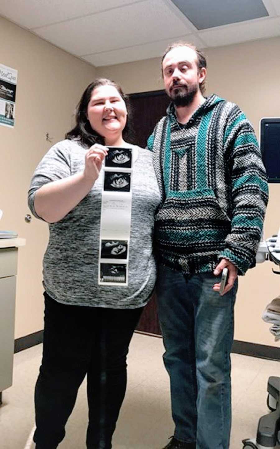 A husband and wife in a hospital room holding ultrasound photos