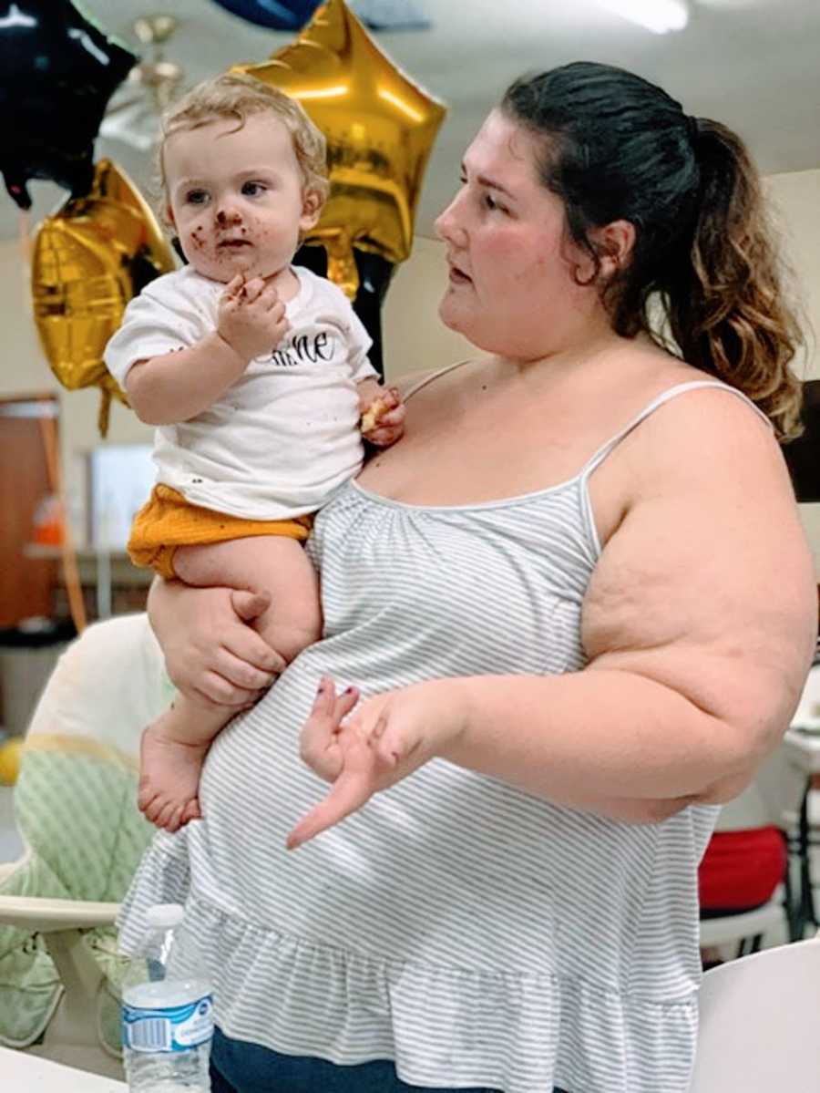 A mother holds her baby in front of balloons