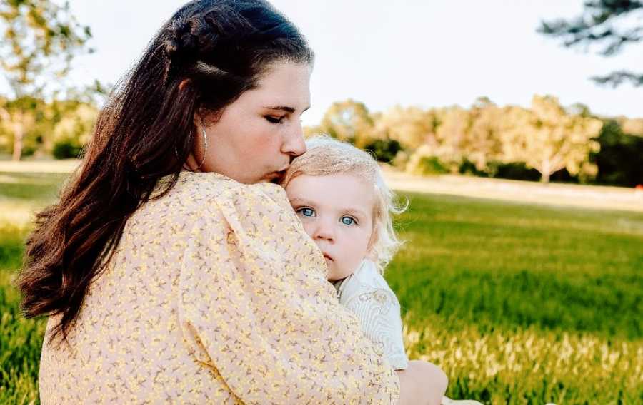 A mother hugs her baby in a field