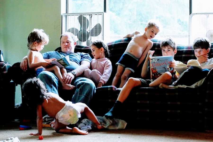 A father sits on the couch with his six children