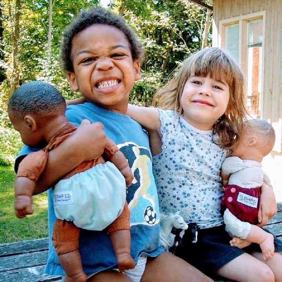 Adopted siblings hold dolls and smile outdoors
