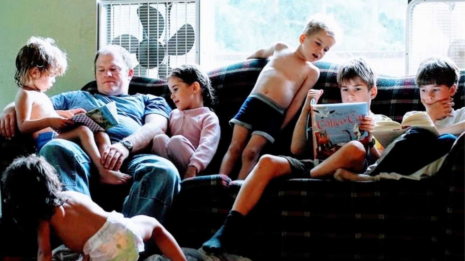 Six kids sit with their father on a couch