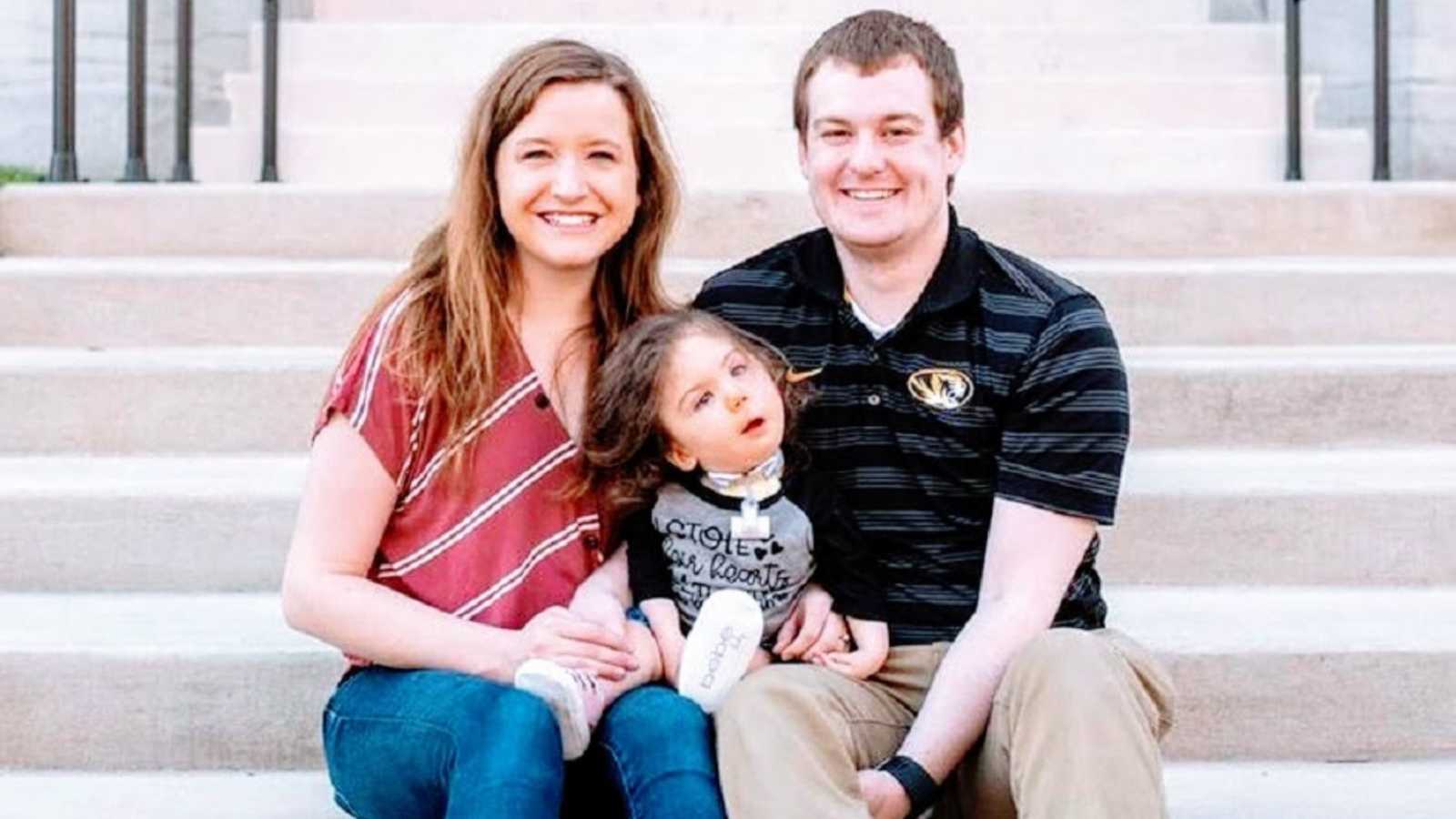 Parents sit with their adopted daughter on courthouse steps