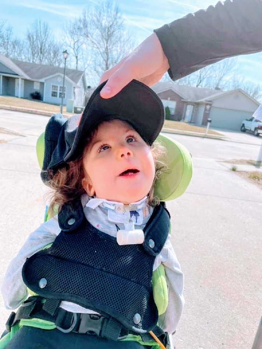 A little girl sits in a wheelchair wearing a hat