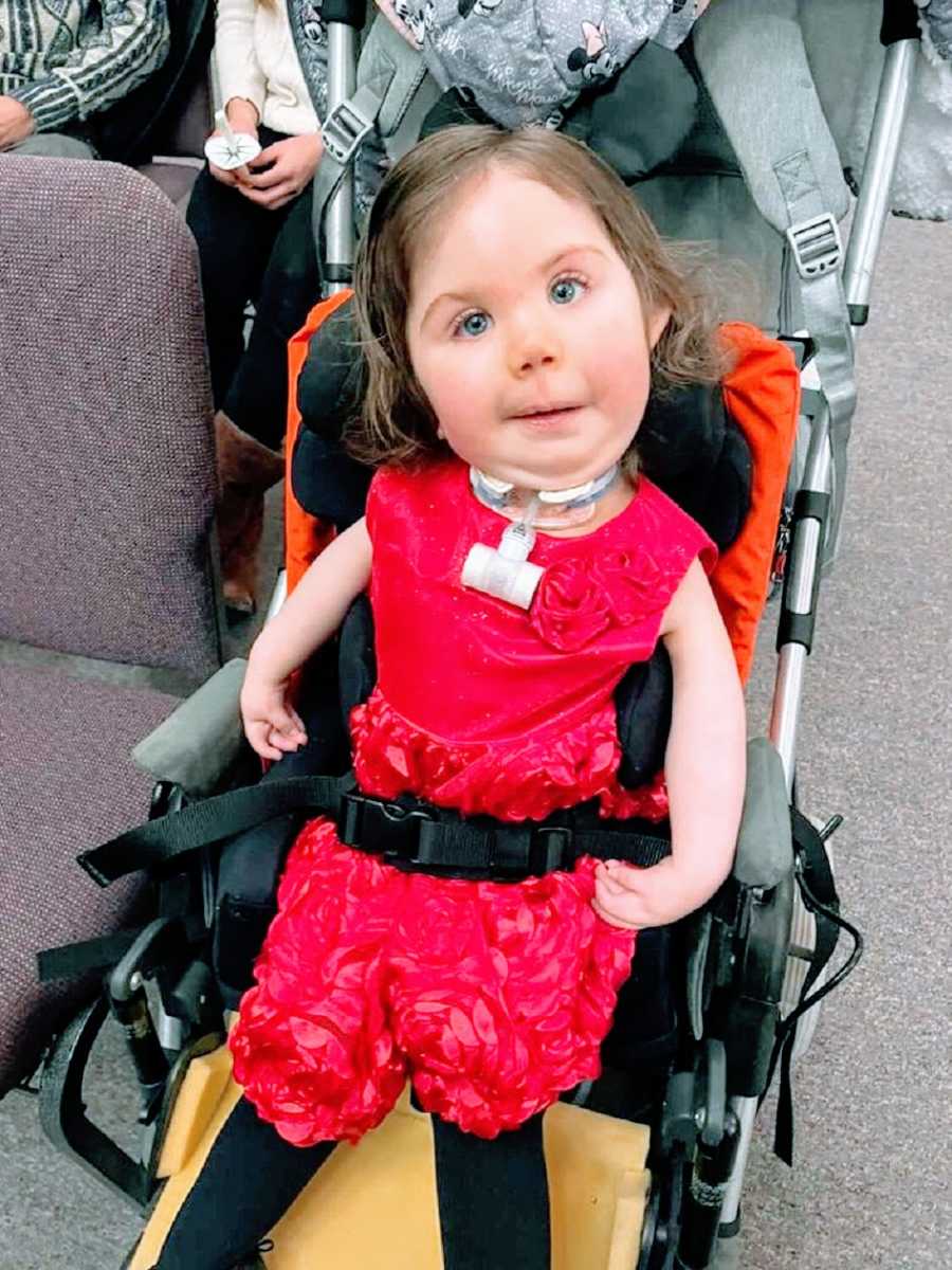 A little girl sits in a stroller wearing a red dress