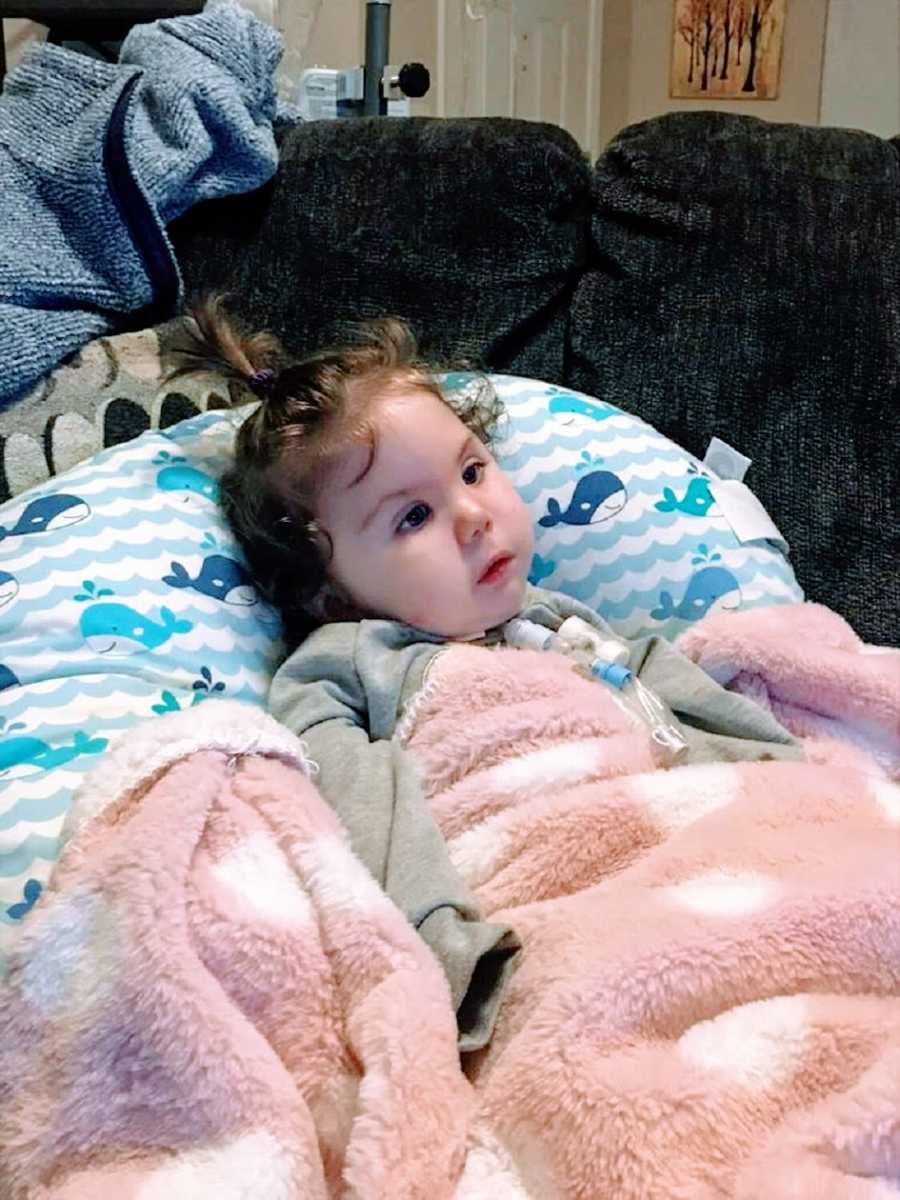 A little girl lies on a pillow and looks off at something