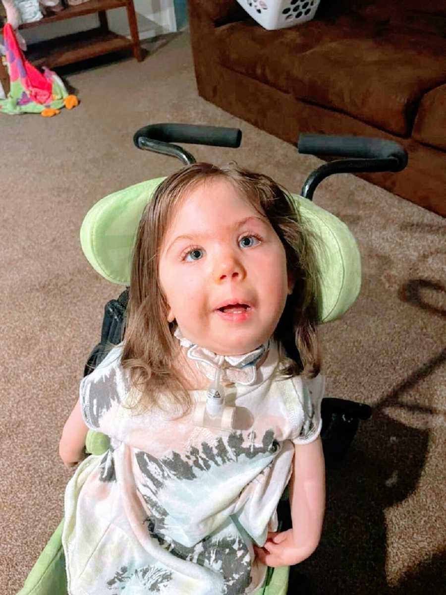 A little girl sits in a green wheelchair