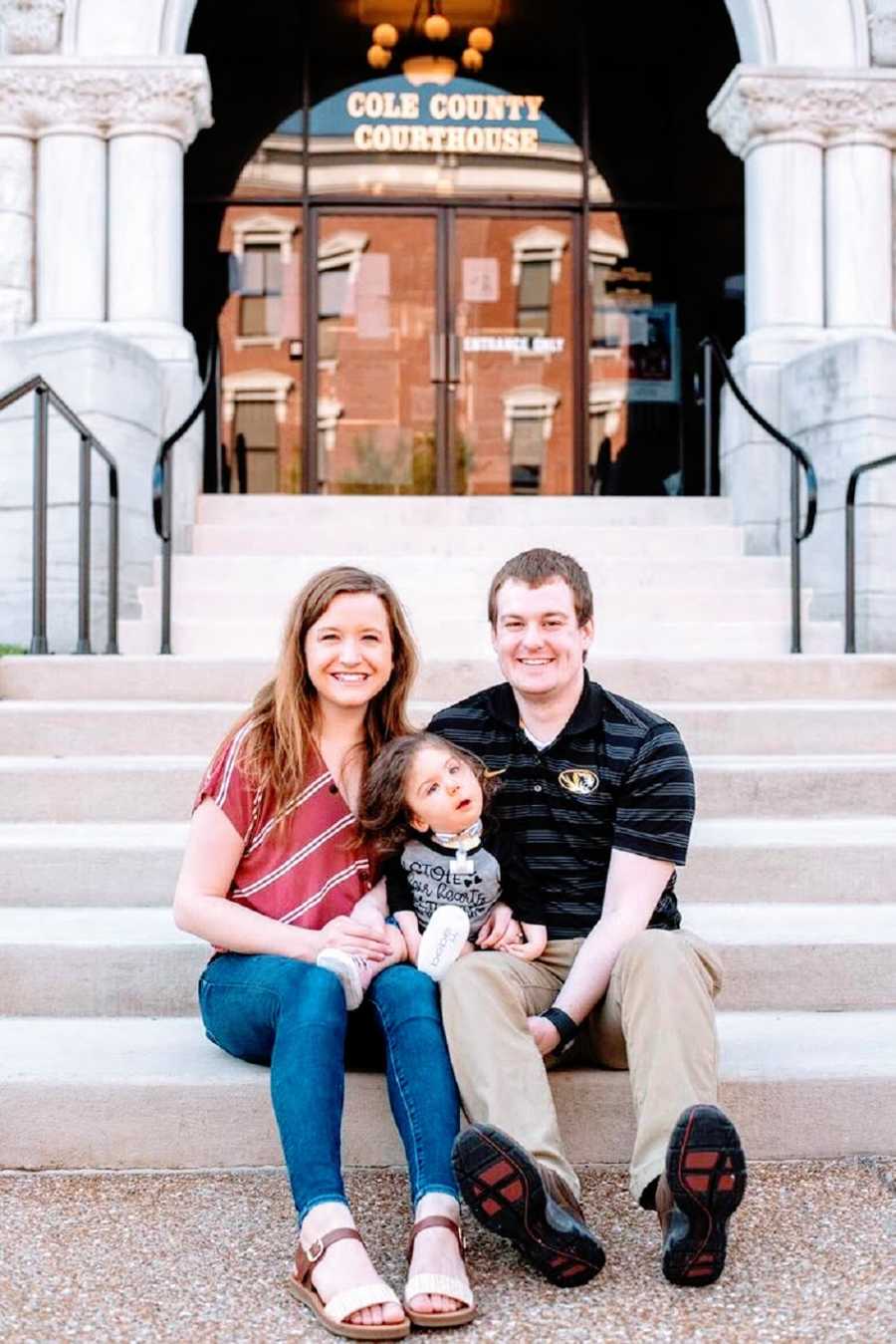 Parents sit on steps with their adopted daughter