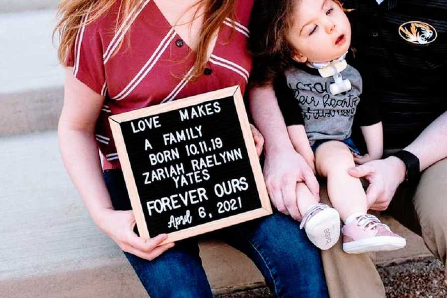 A mother sits holding a sign with her baby girl