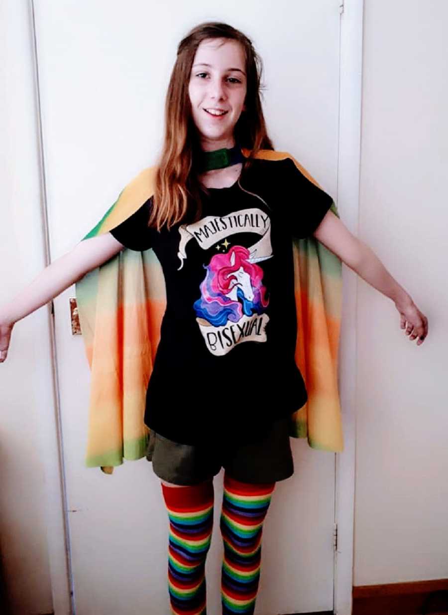 A bisexual child wearing a pride shirt and a cape