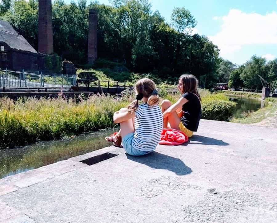 Two children sit together by the water