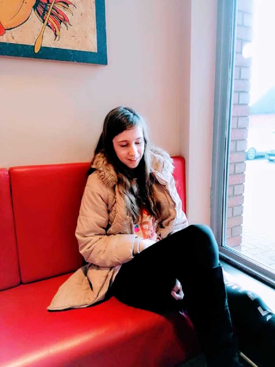 A child sits in a red seat wearing a coat