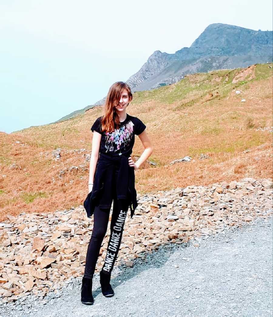 A child wearing black leggings and a black shirt stands outside