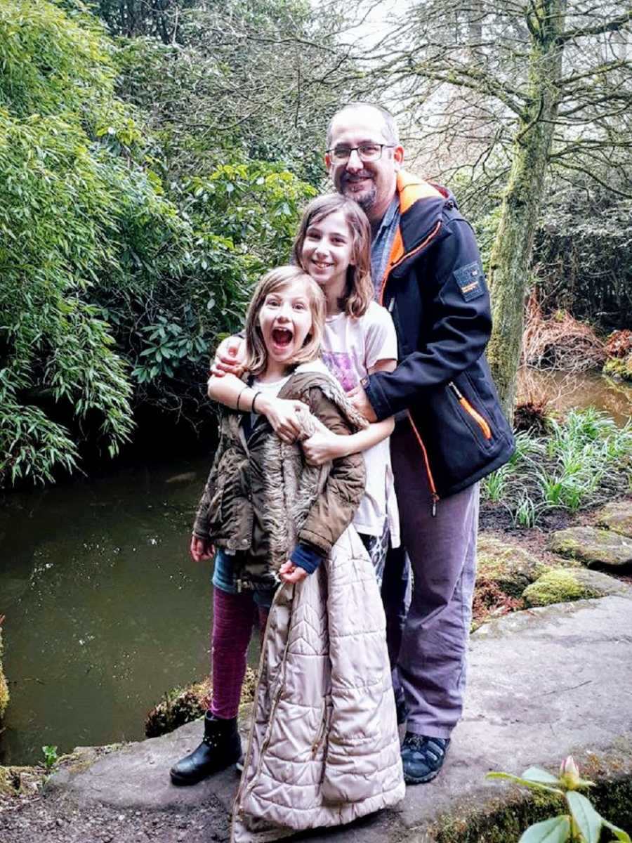 A father stands with his two children on a rock in a pond