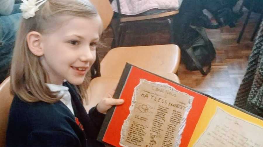 A girl with autism holds up a school project at her desk