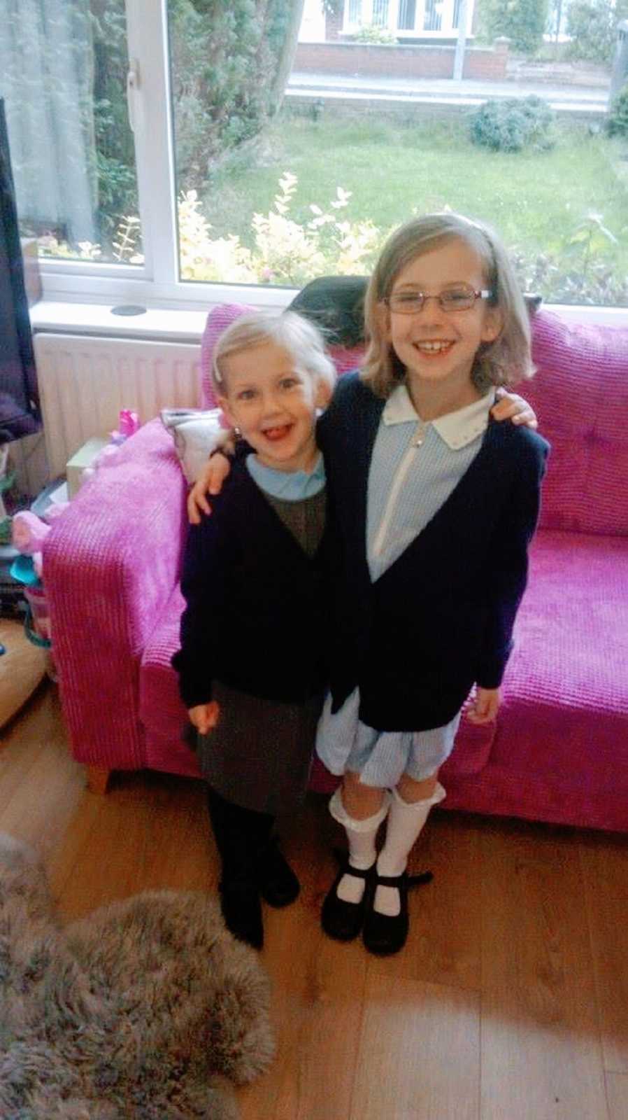 A pair of siblings stand together wearing school uniforms