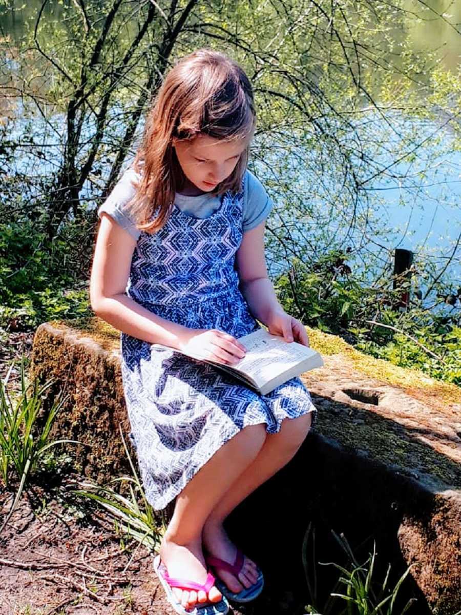 A girl in a blue dress reads a book outside