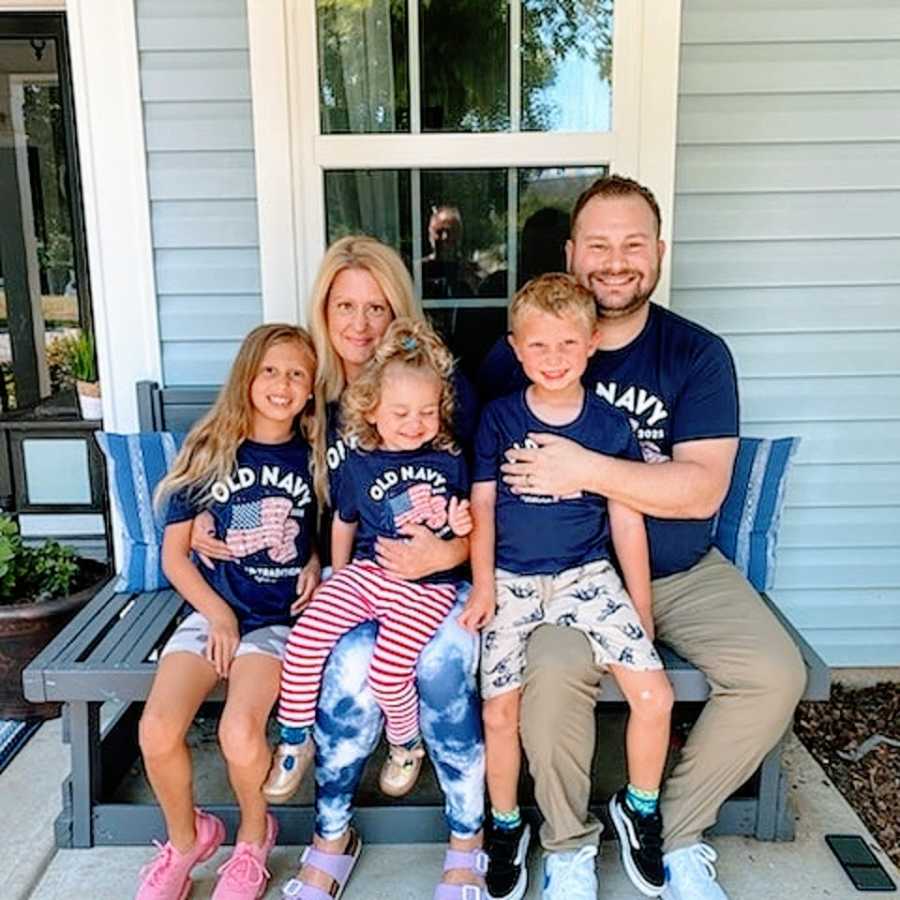 A couple sit on a bench with their three children