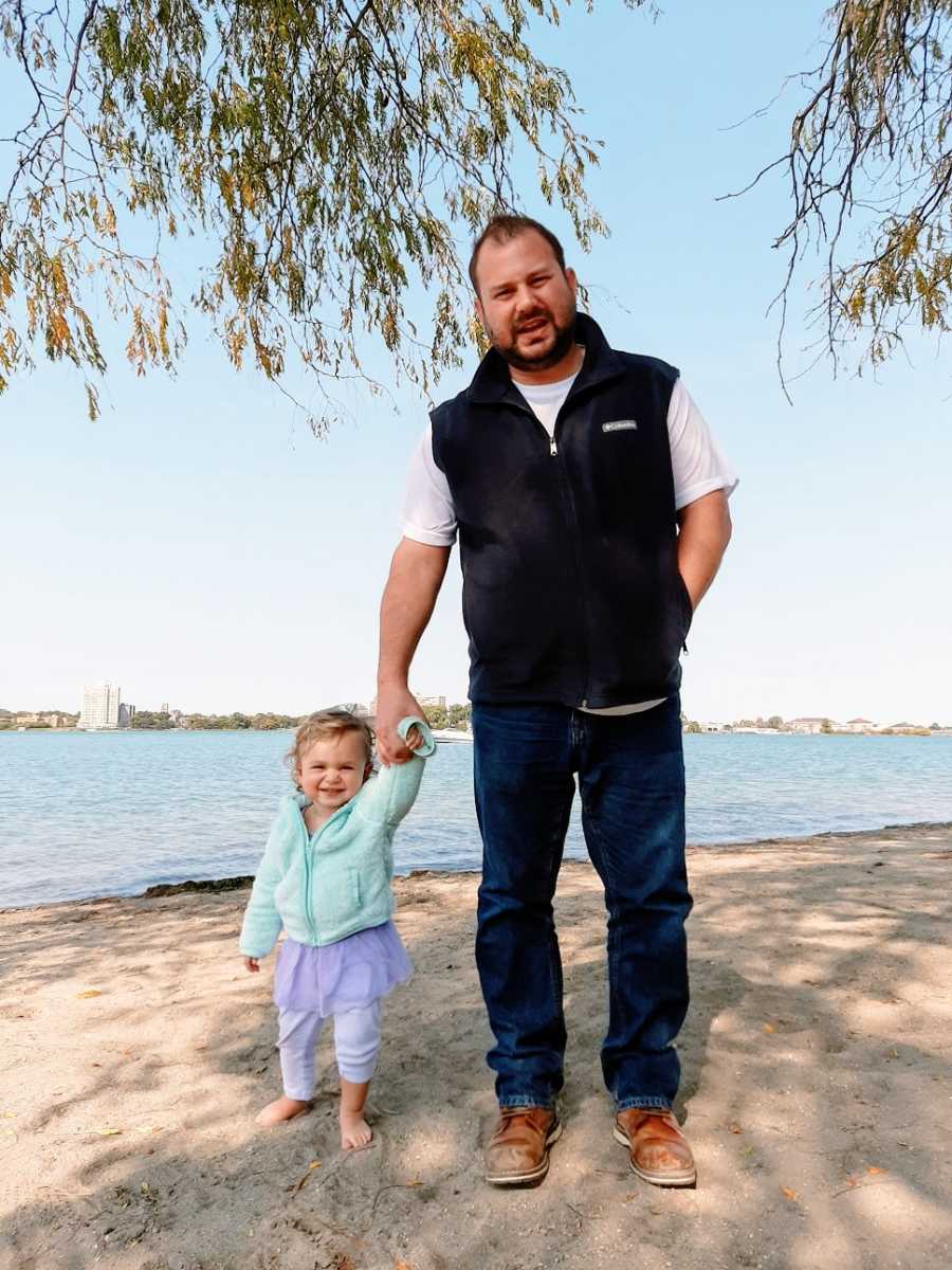 A man holds his young daughter's hand by the water