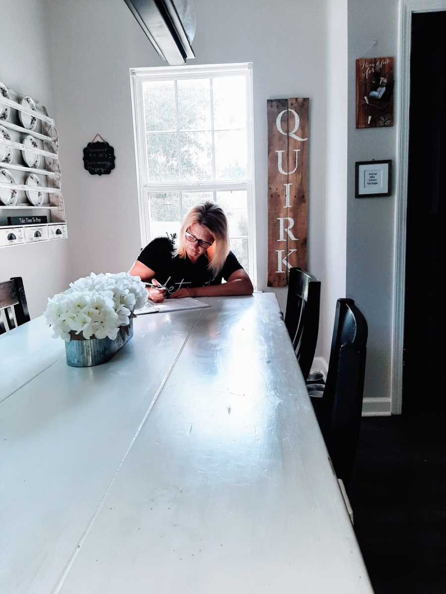 A woman sits at a long table writing