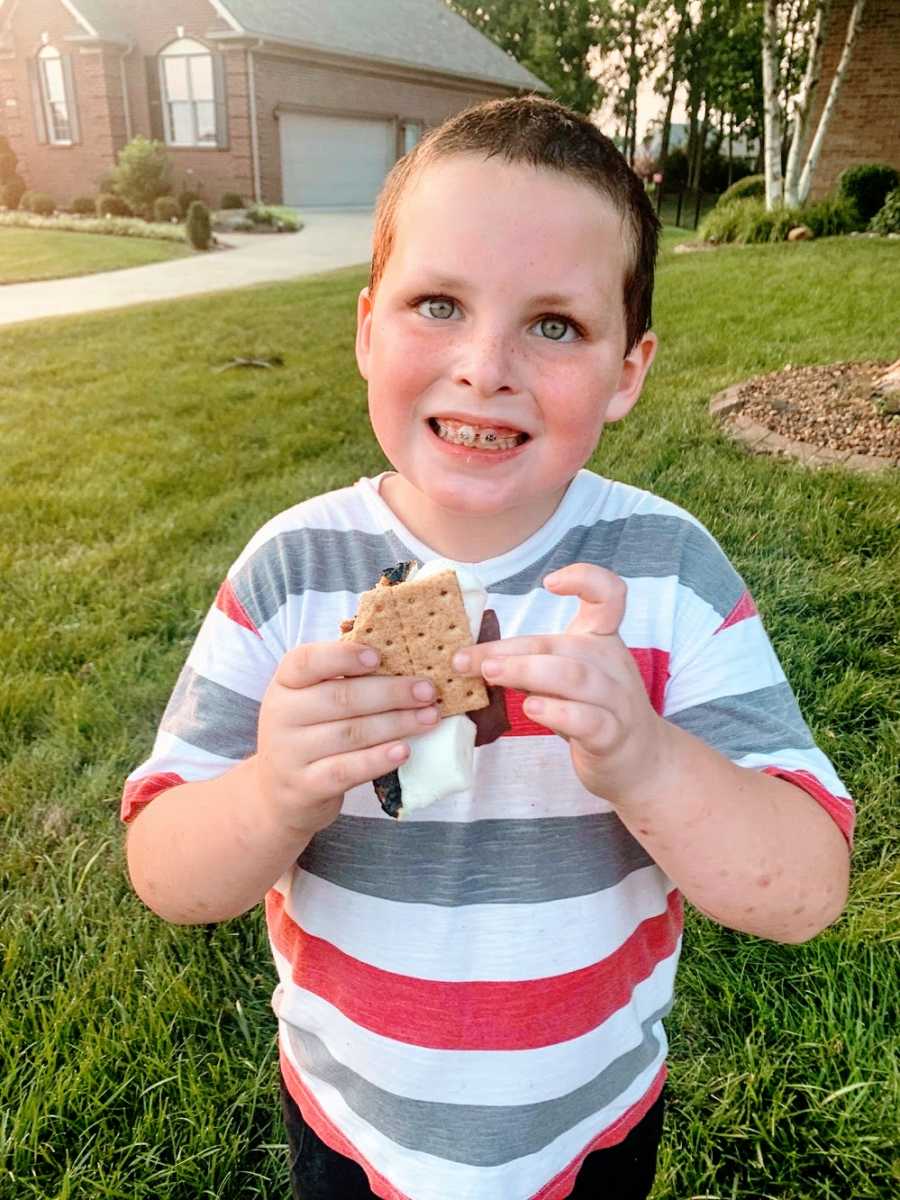 A boy with braces smiles while holding a s'more