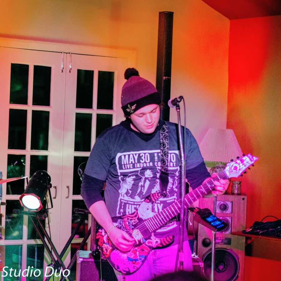 A man plays guitar while wearing a hat indoors