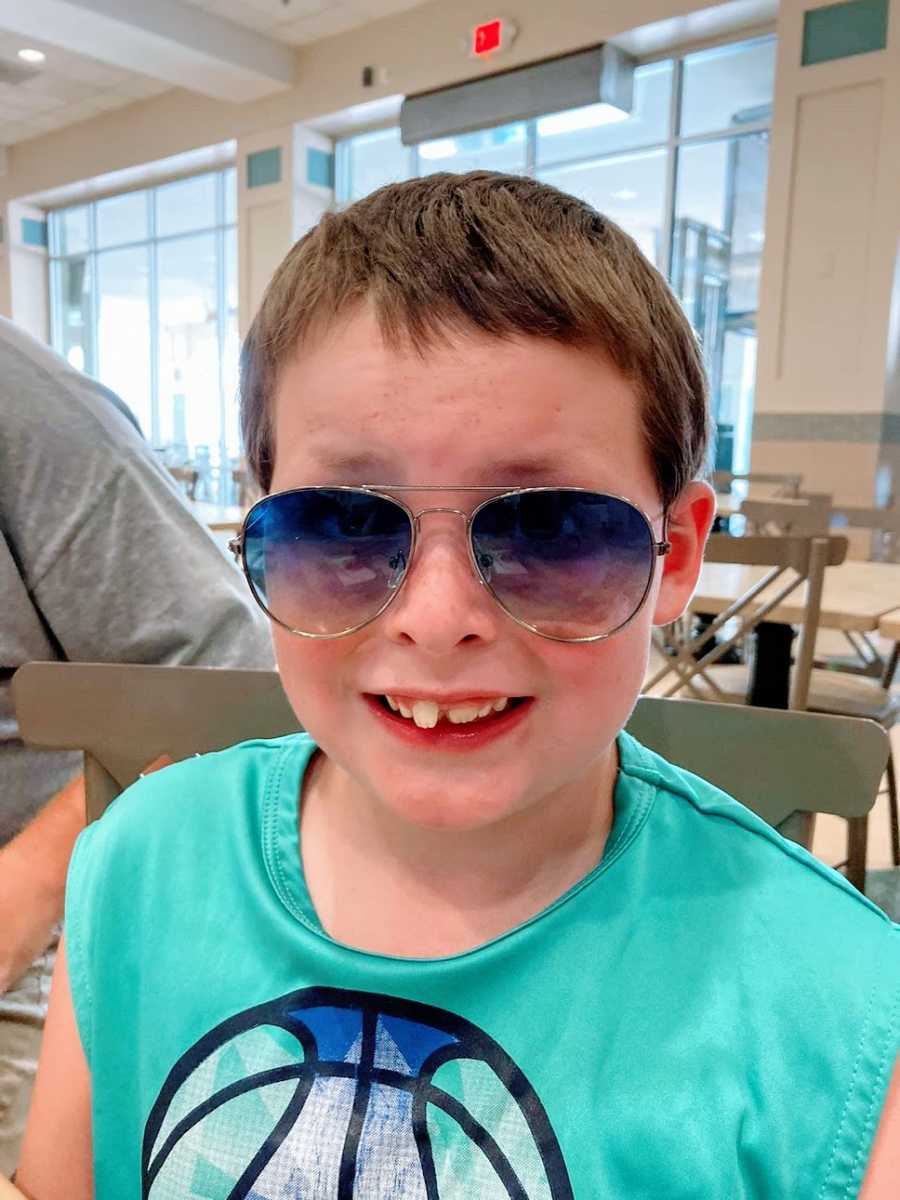 A boy wearing sunglasses sits in a grey chair