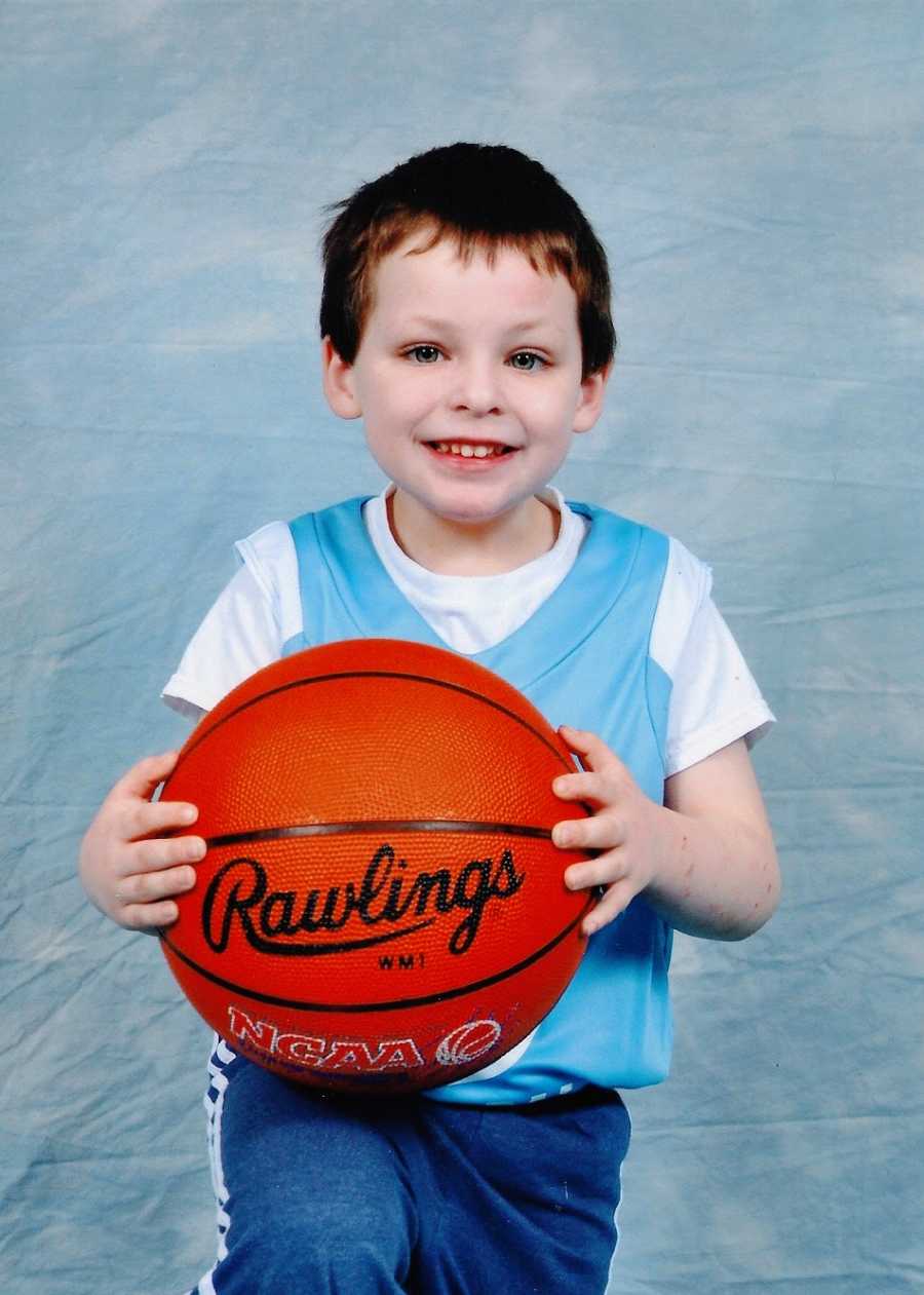 A little boy sits holding a basketball on his lap