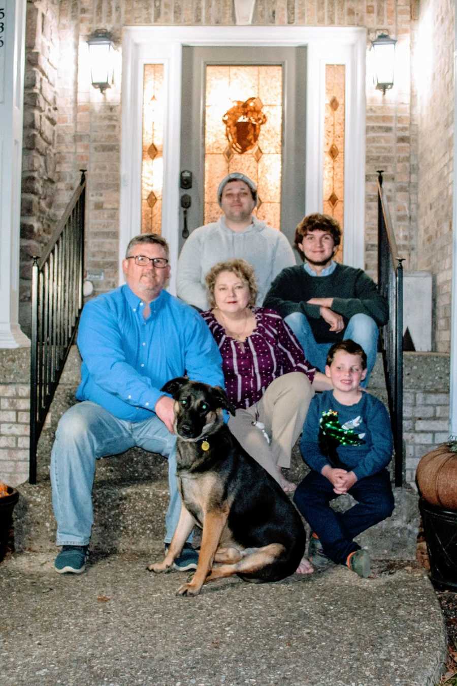 A family of five sit with their dog on their front steps