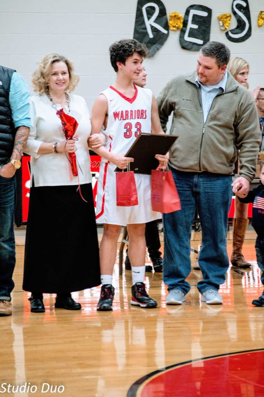 Parents stand in a gym with their son who wears a basketball uniform