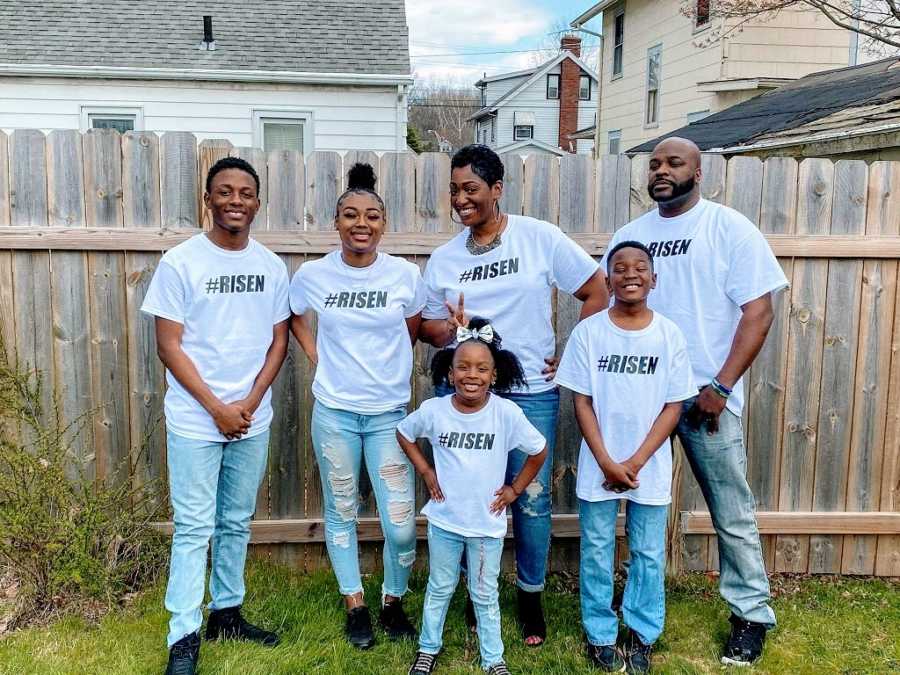 A family of 6 stand together wearing matching shirts