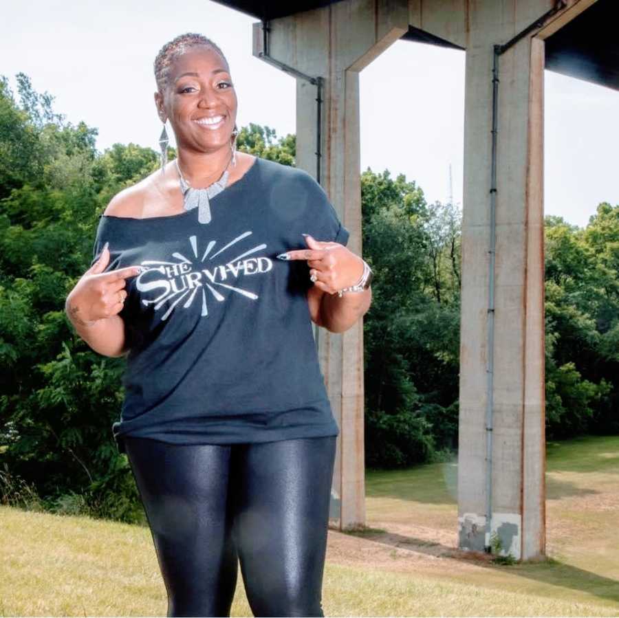 A woman points to her black shirt that says "She Survived"