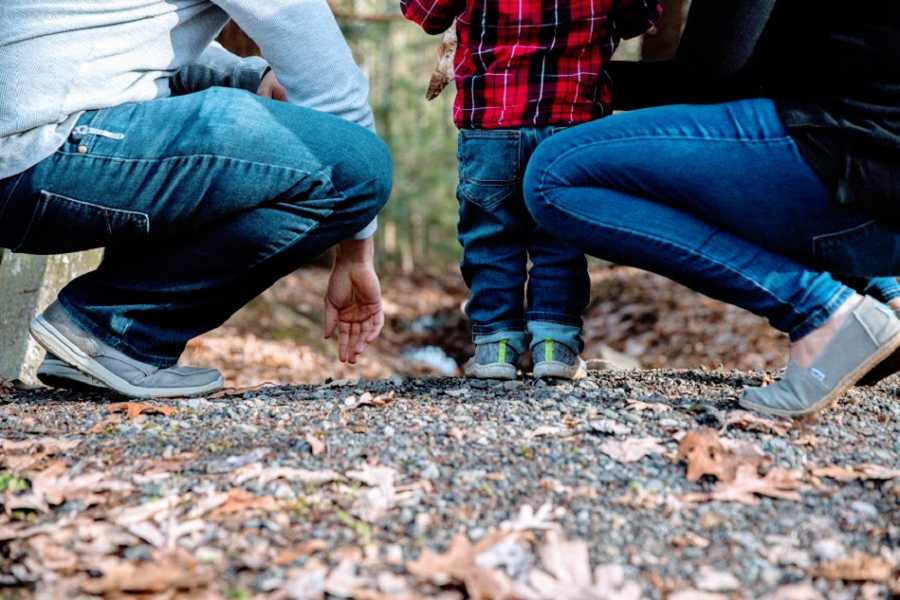 Parents kneel on the ground near a boy in a red plaid shirt