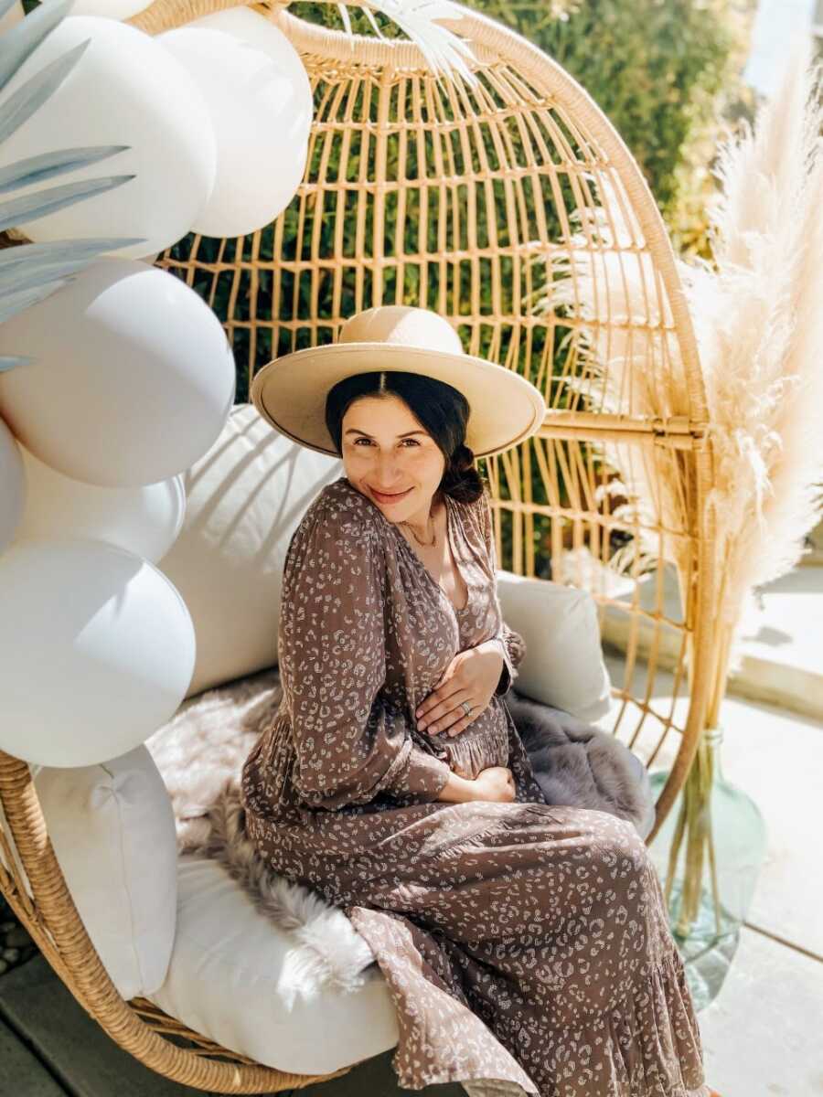 Woman expecting her fourth child takes pregnancy announcement photos in an animal-patterned dress while sitting in her backyard