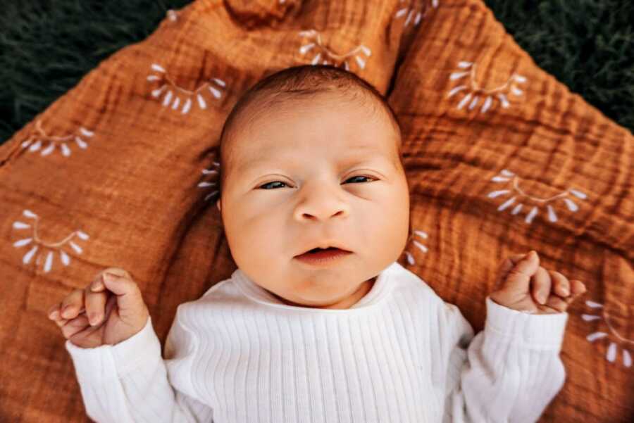 Mom takes a photo of her newborn son named Sonny laying on a blanket with suns on it while wearing a white sweater