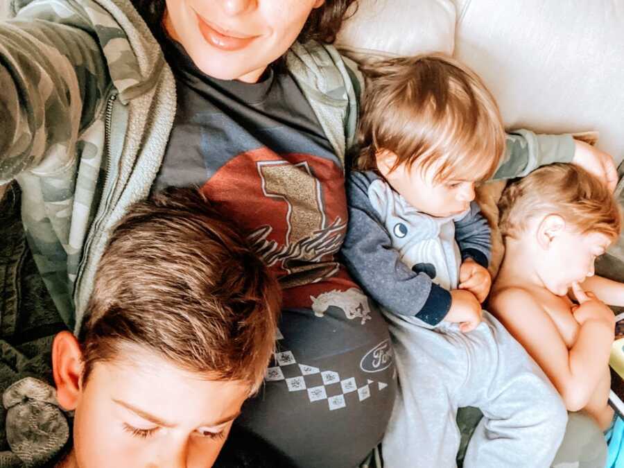 Heavily pregnant mom cuddles with her three sons on the couch