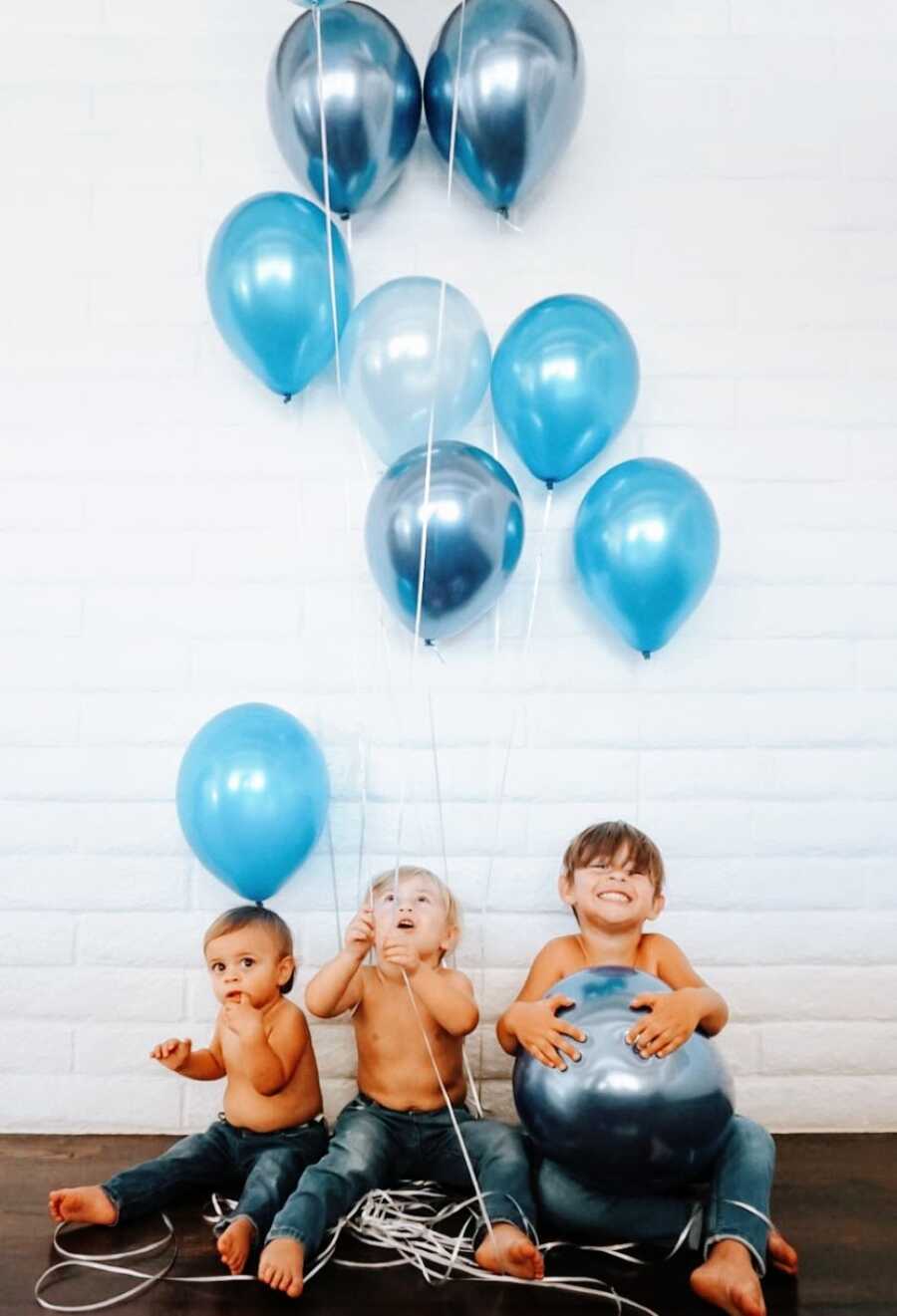 Couple expecting their fourth baby announce the gender by taking a photo of their three sons holding blue balloons