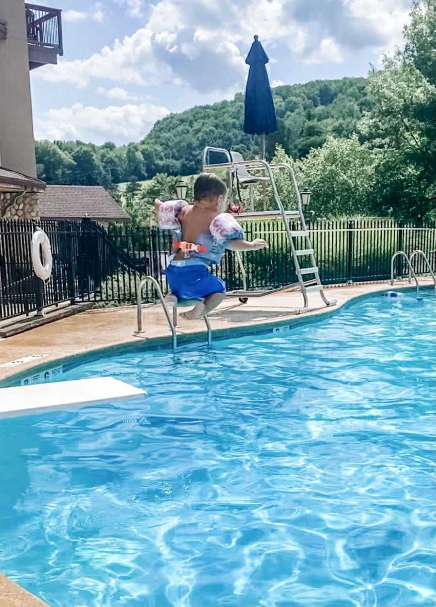 Little boy jumps off diving board during a summer pool day wearing floaties