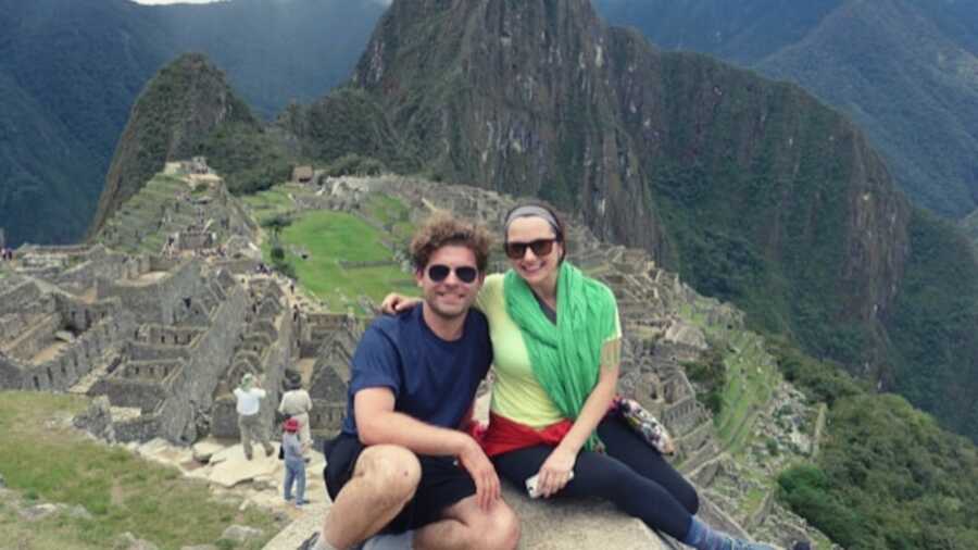 Woman in green scarf and man in blue shirt sitting on top of mountain