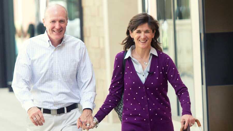 Wife in purple sweater holding hands with husband in white button down