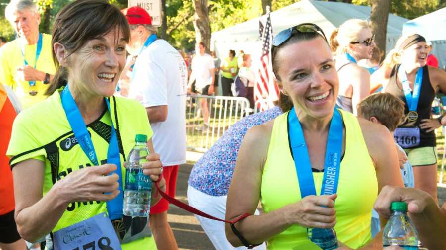 Two women in neon yellow shirts holding water bottles at start line of marathon