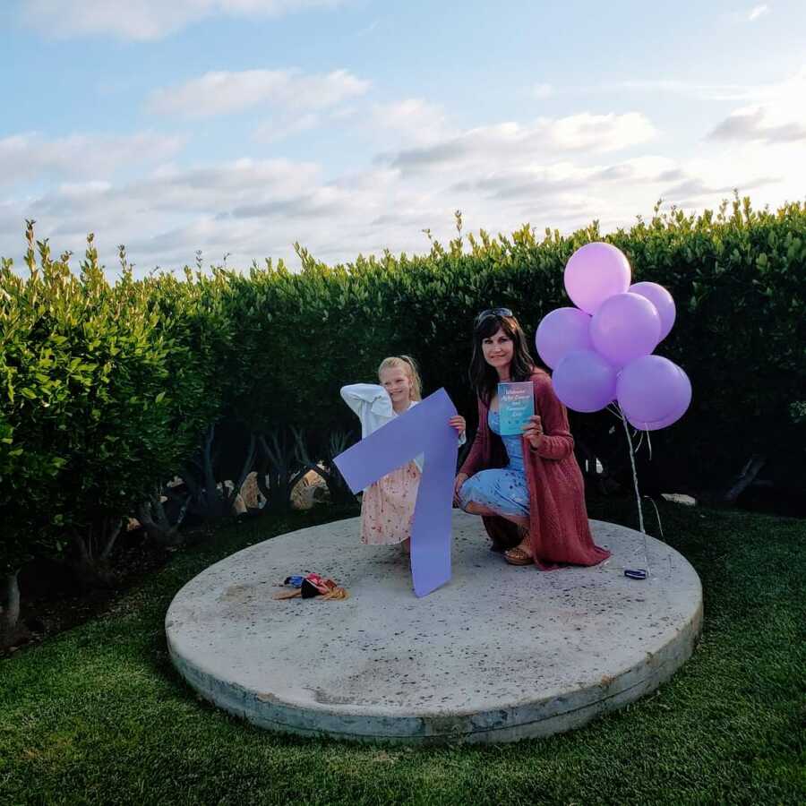 Mom of 4 celebrating surviving choriocarcinoma cancer for 7 years poses with one of her daughters with a big 7 and balloons